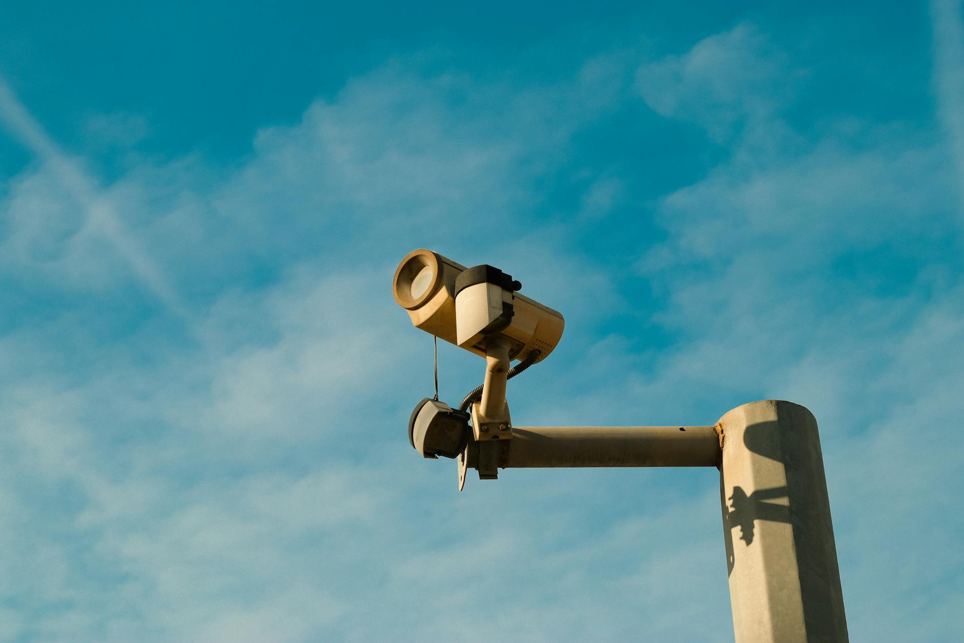 A surveillance camera mounted outdoors against a bright blue sky, symbolizing security and monitoring.