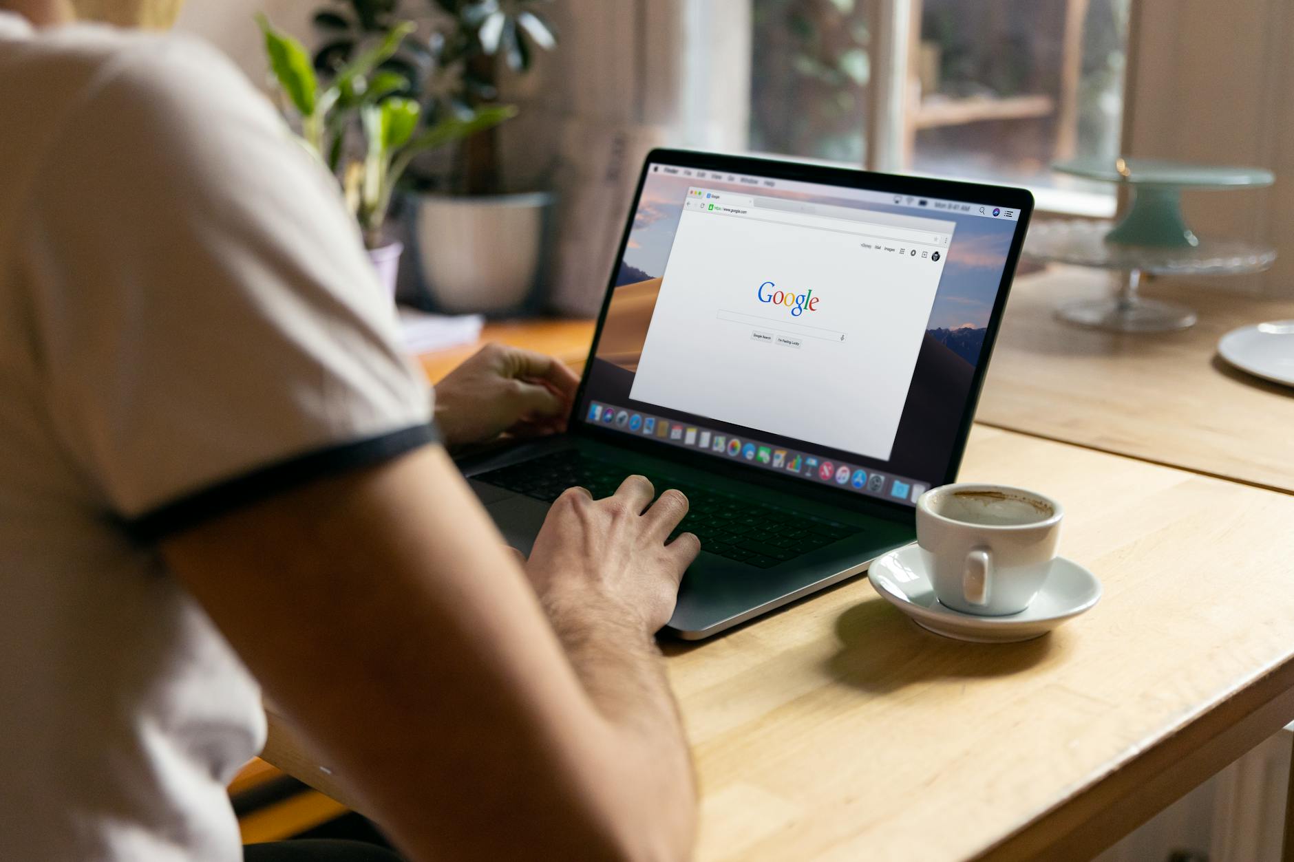 A person working on a laptop in a cozy indoor setting with a coffee cup on the table.