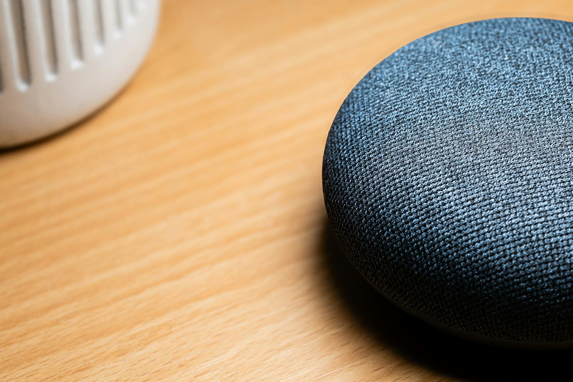 A close-up view of a smart speaker on a wooden table, capturing texture details.
